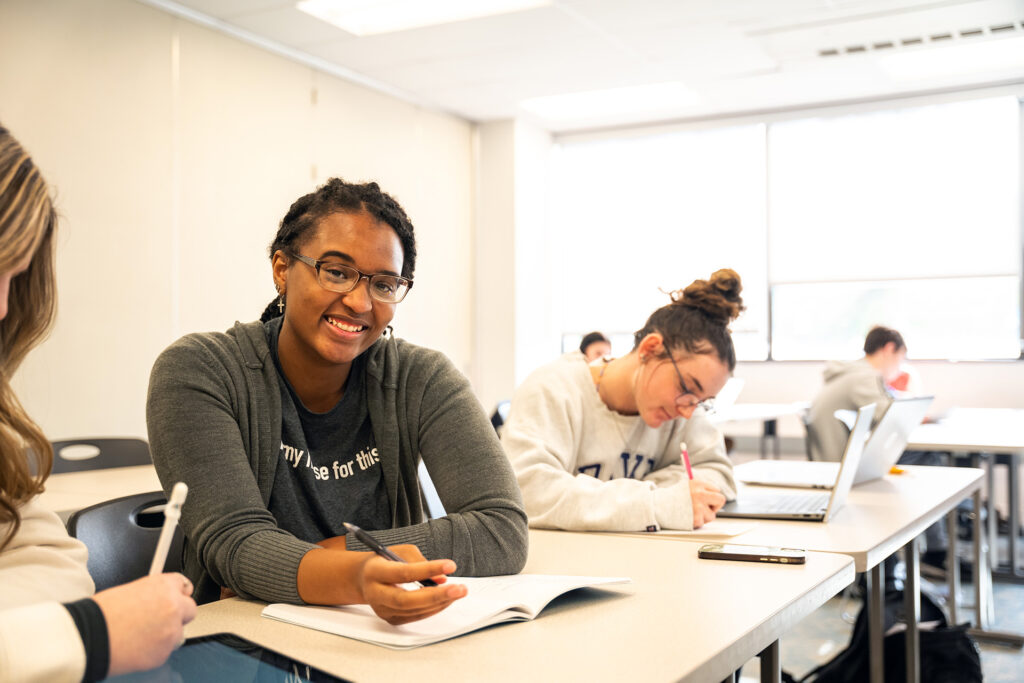 A female student smiling with other students in the background learning